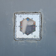 A grey concrete wall with a metal square box fitted into it — the time capsule. Etched into its surface is a hexagon with flags and wording too small to make out.