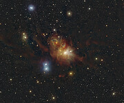 This image shows stars and clouds of gas and dust distributed over a dark background. A prominent cloud of gas and dust can be seen in the central part of the image. It features an amorphous cloud in a red, brown and yellow hue. Several brightly shining stars in blue and yellow can be seen around the cloud.