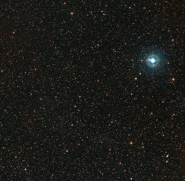 The image shows a dark area of night sky, speckled only lightly with the white and blue glow of stars. Towards the upper right region of the image there is a large bright blue star which stands out among the others.