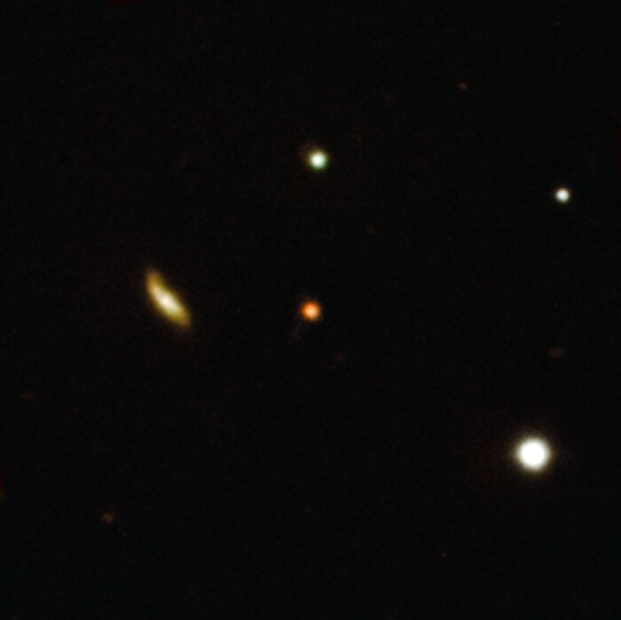 This image shows a few bright points, coloured in white and yellow. These are galaxies. Right in the middle, there is a red point, which is an extremely distant explosion in a galaxy in the early universe. The background is completely black.