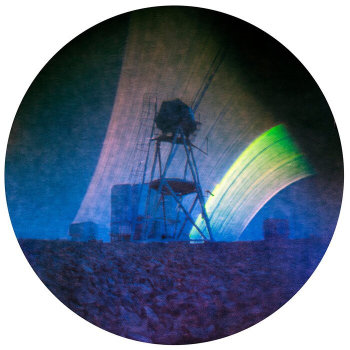 This Picture of the Week has a circular shape and has a grainy texture. The lowest third of the image shows the ground upon which the telescopes stand. A tall metallic structure is a the centre of the image. Behind it there are several telescope domes. The uppermost two thirds of the image is covered with the dark blue sky. In the sky are large strips of coloured lines. The leftmost part of the strips are colored in light red, and the rightmost part in yellow. Among the coloured lines are a few dark streaks.